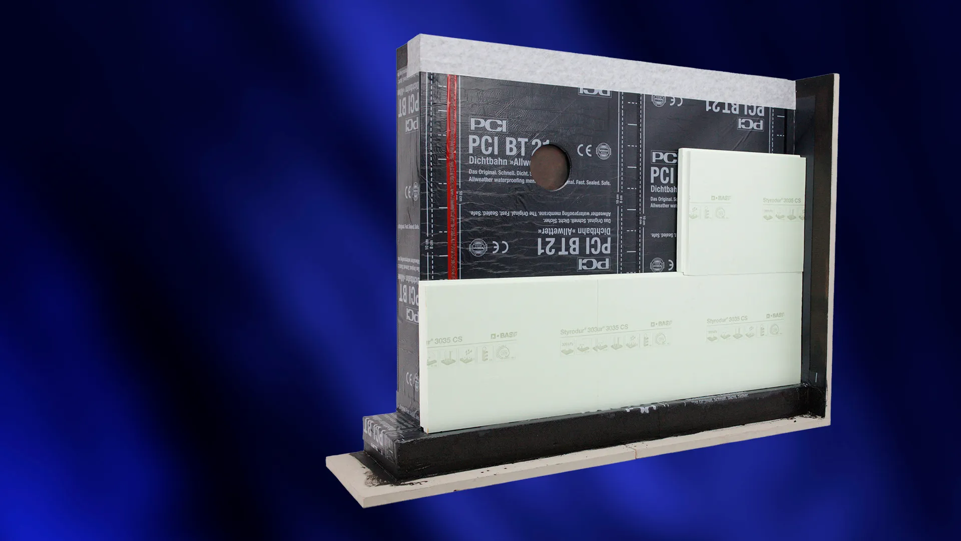 Wandmodell mit schwarzer PCI-BT-21-Dichtbahn, teilweise angebrachten hellen Dämmplatten und runder Öffnung vor blauem Hintergrund.